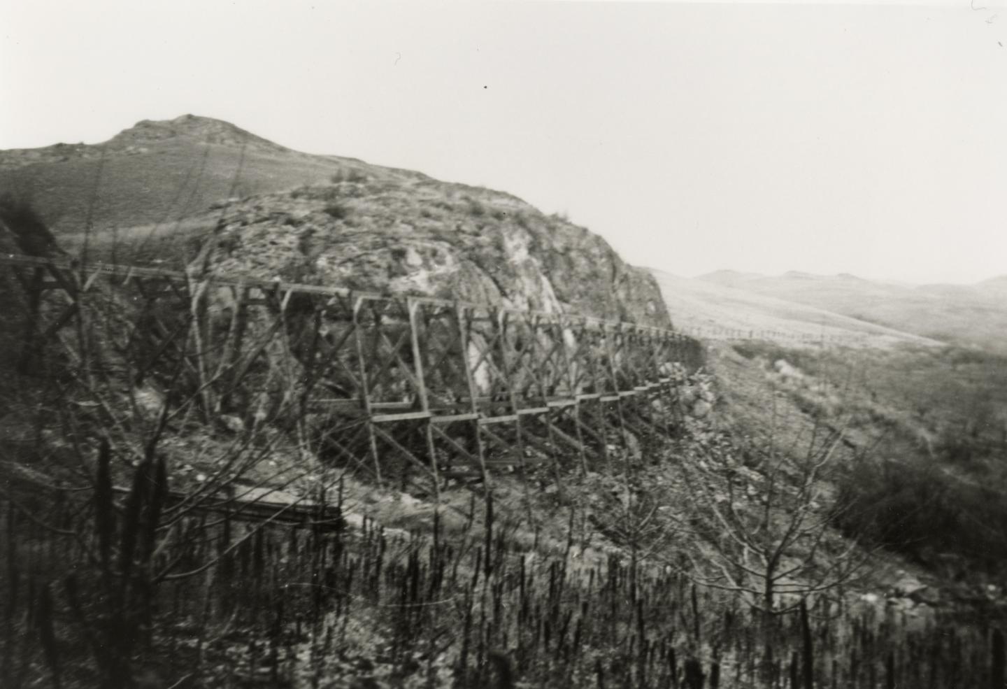 Black and white photo of a wooden trestle bridge on a rocky hillside.