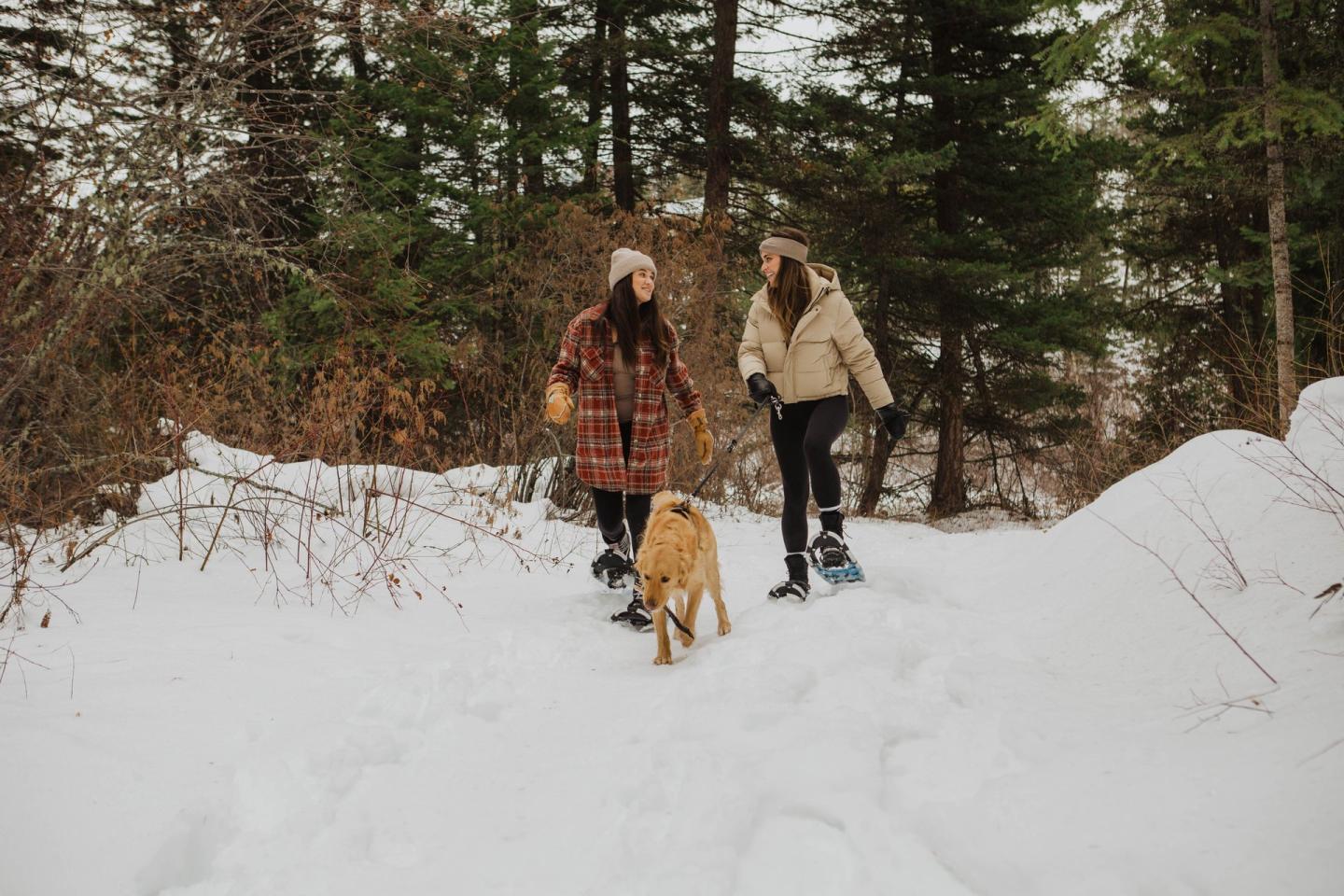 women snowshoeing through the forest with a dog