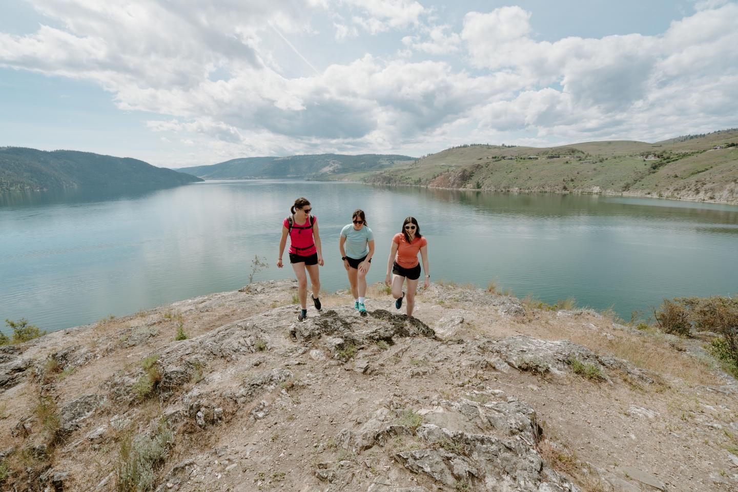 Three people walking on a mountain by a lake