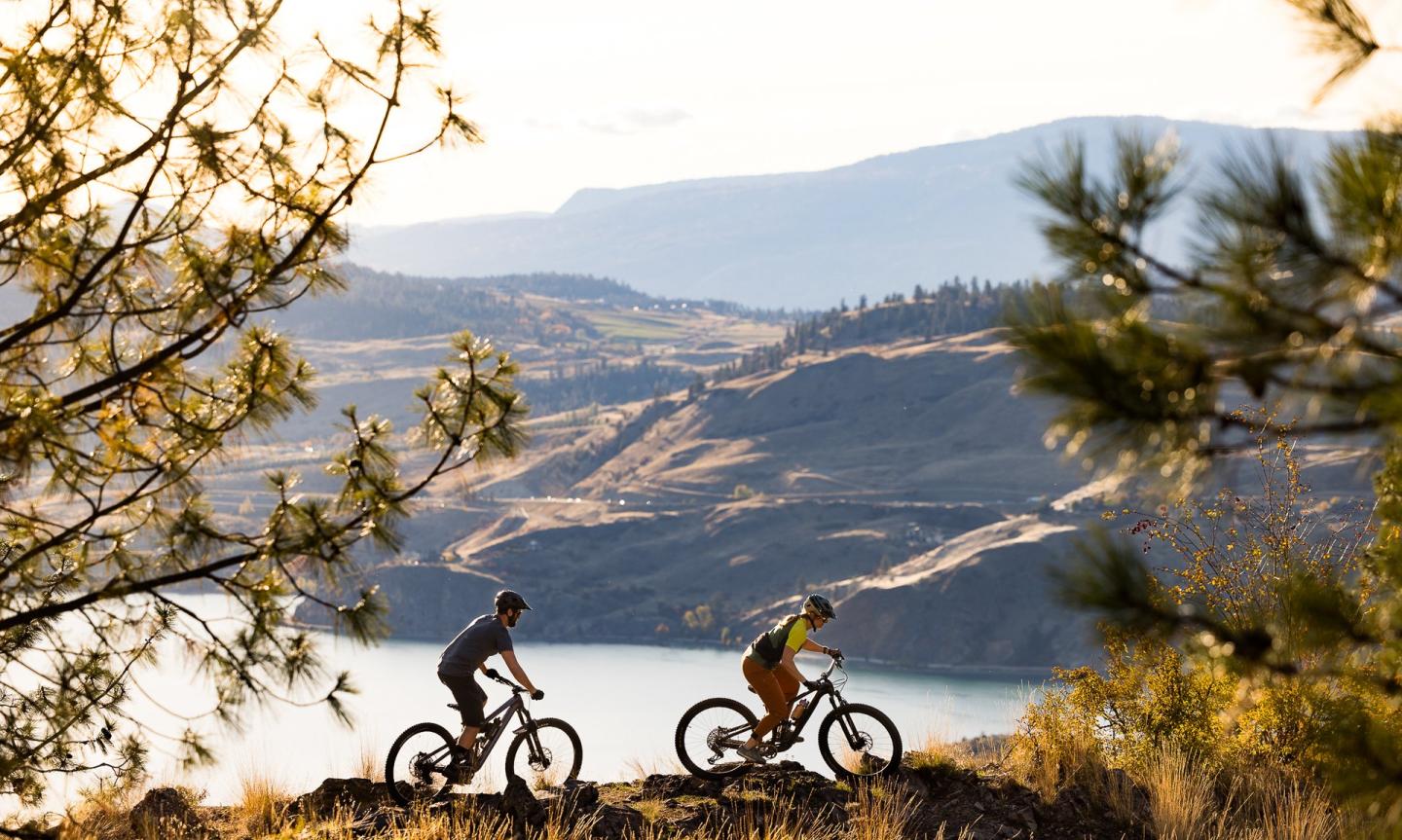 mountain bikers traversing a trail overlooking kalamalka lake