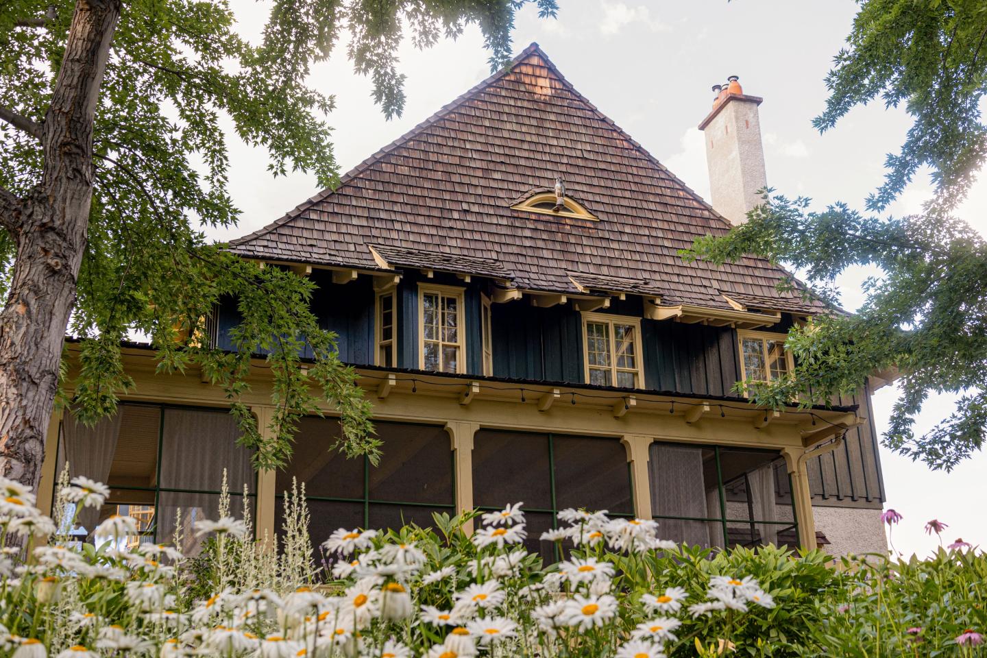 Historic house with steep roof, surrounded by trees and daisies.