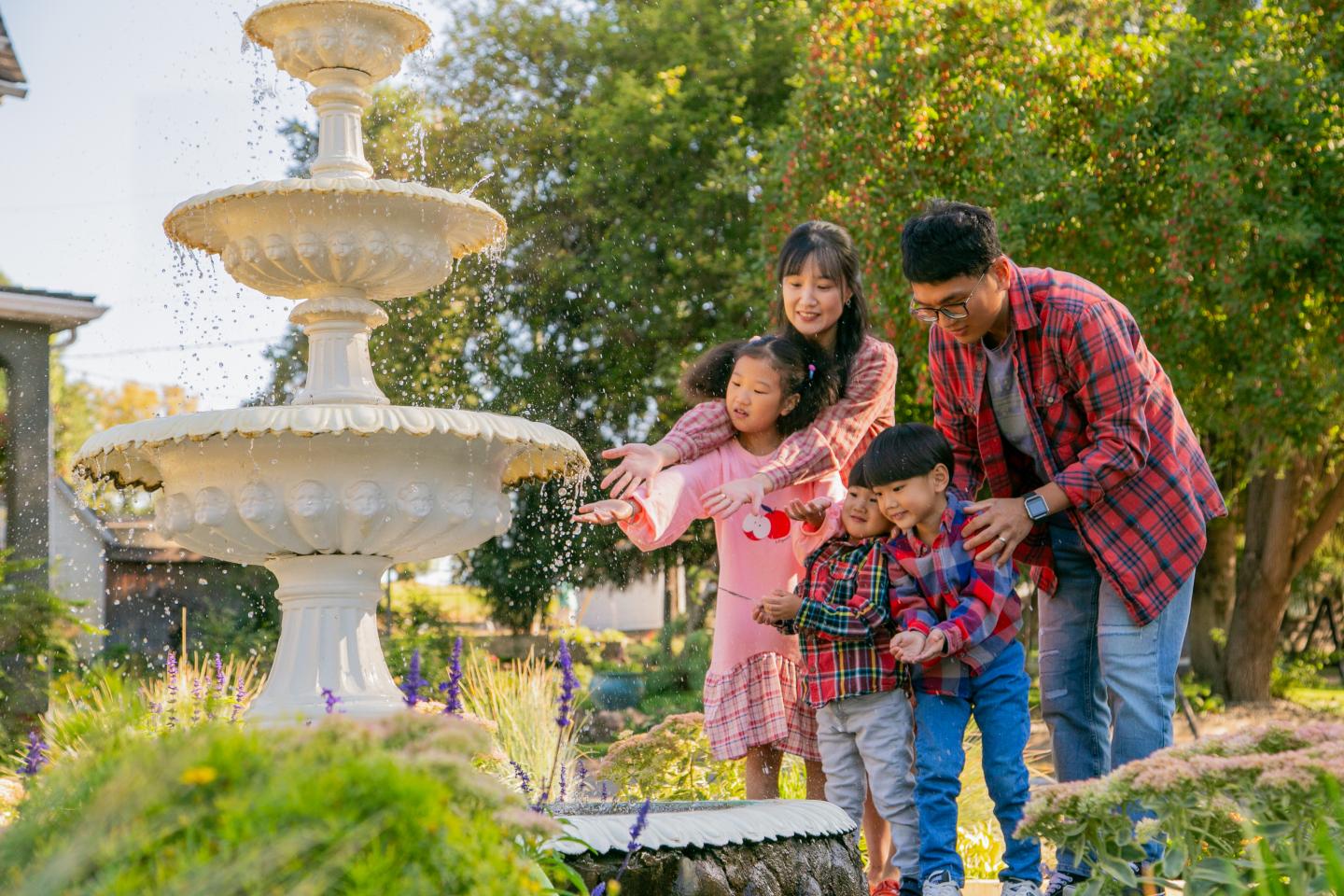 Family with two children near a fountain in a garden, smiling and playful.