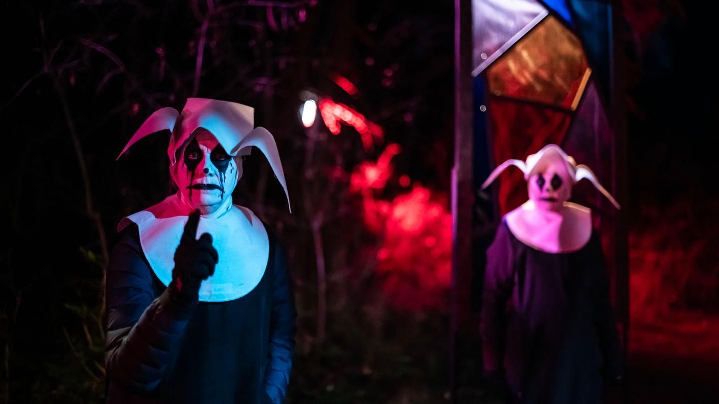 Two masked figures with dramatic lighting in a dark, eerie setting.