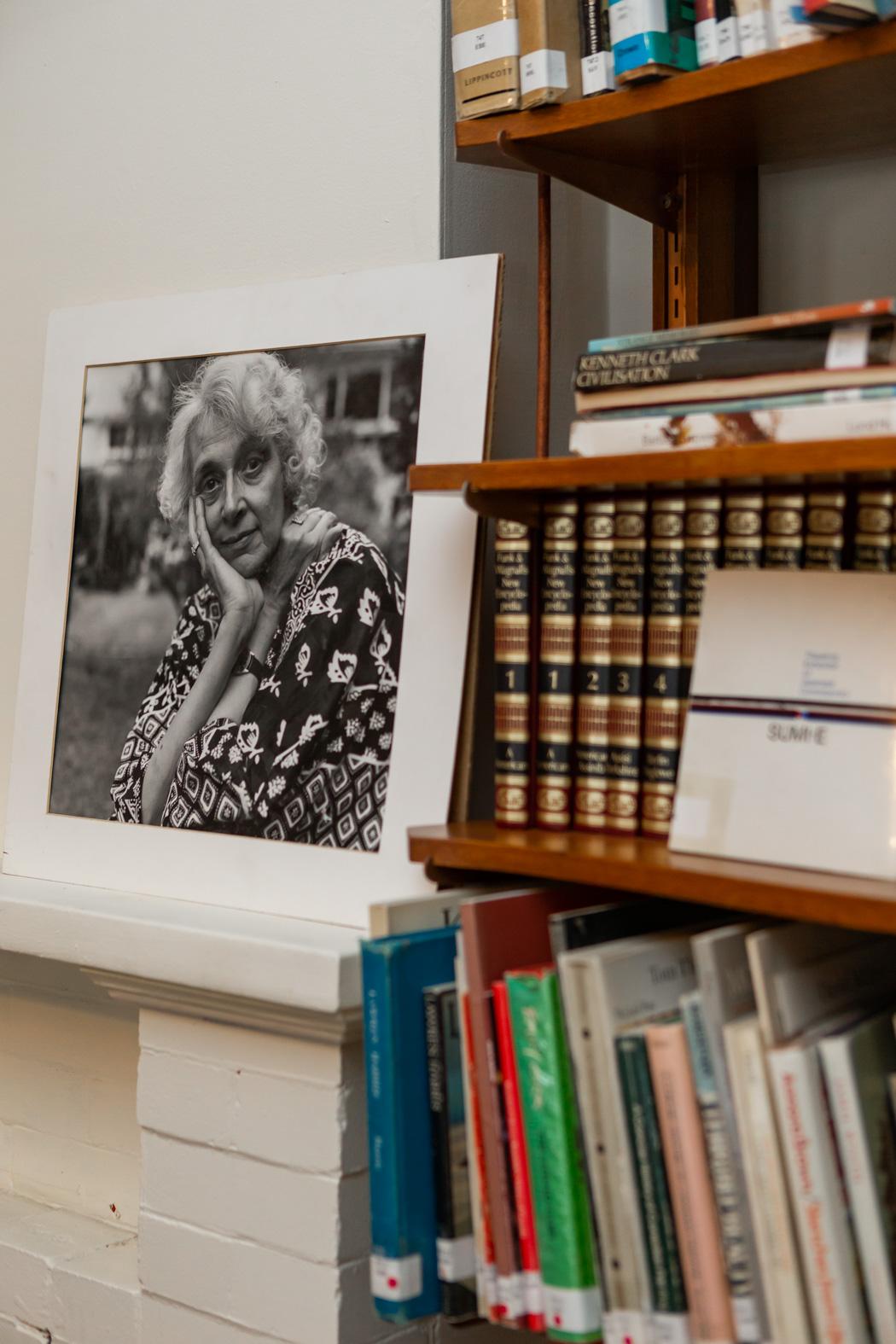 Black-and-white portrait of a smiling elderly person near a bookshelf.