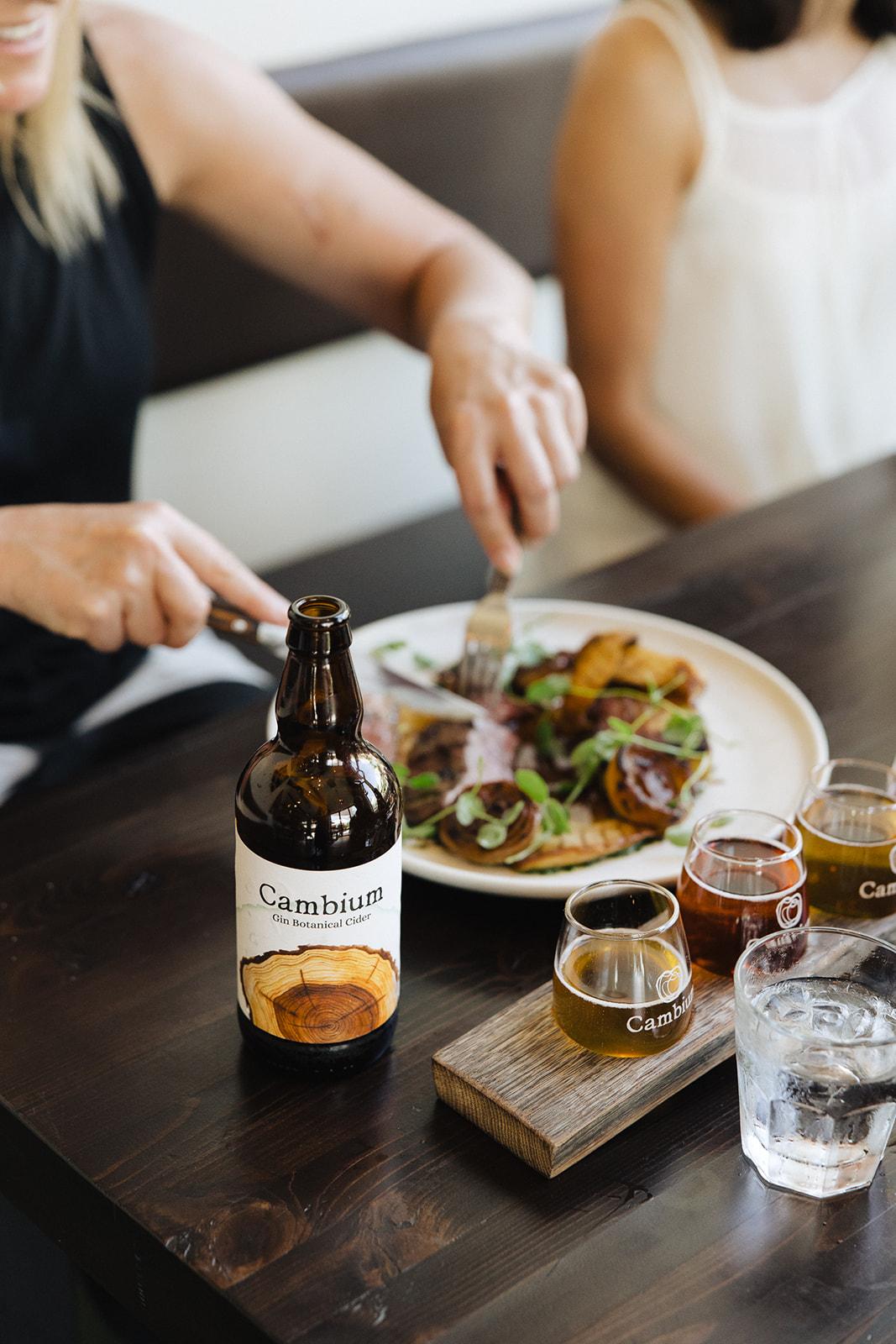 Dining setting with a plate of food, beverages, and someone cutting food.