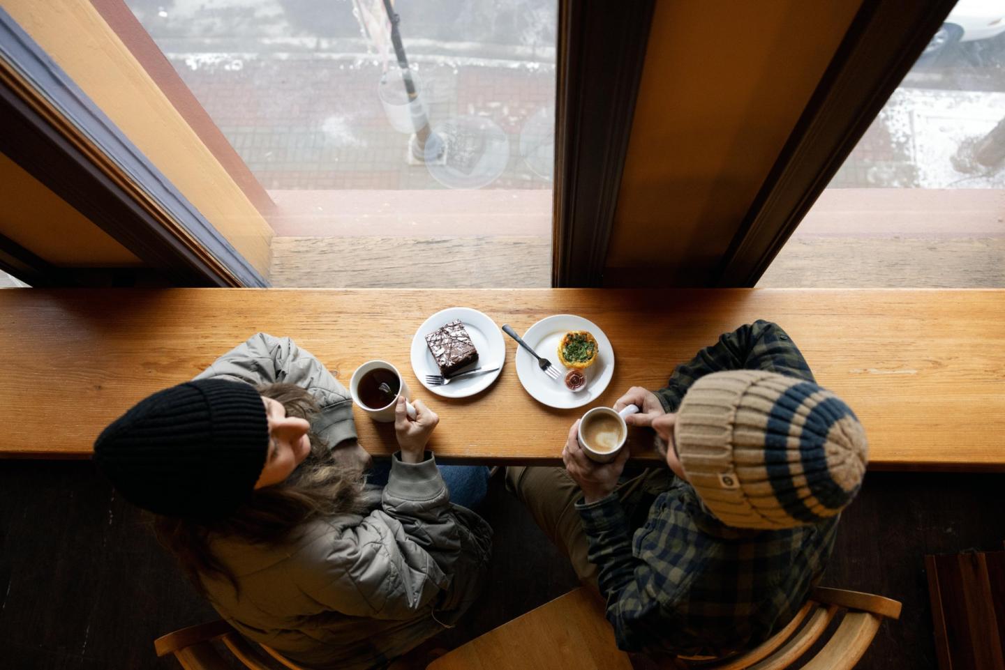 Cozy café above view, two people with drinks and pastries by the window.