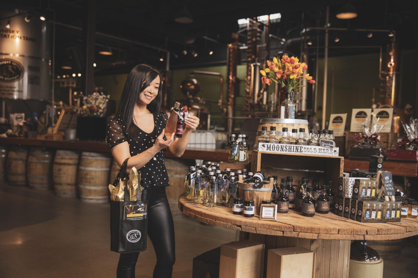 Woman examining a bottle in a distillery shop with wooden barrels.