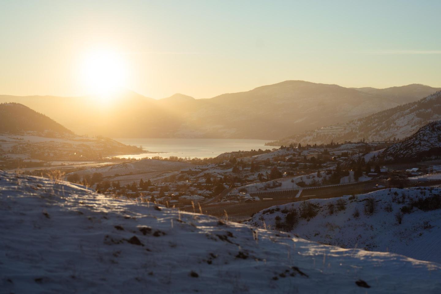 Snowy landscape at sunset with mountains in the background.